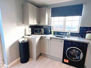 A compact kitchen with a washing machine, a microwave, and a sink. - Elegant 4BDR Home with Private Parking in Darfield (Darfield)