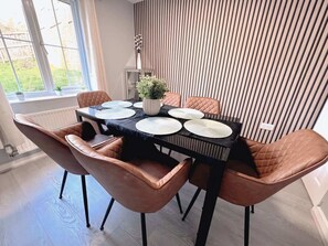 A dining area with a table set for four, surrounded by cushioned chairs, a potted plant, and a striped wall. - Elegant 4BDR Home with Private Parking in Darfield (Darfield)