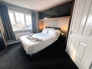 Habitación de hotel con cama, ventana con cortinas, radiador y mesita de noche con lámpara.