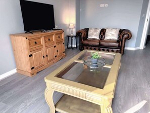 Una sala de estar con un mueble de madera, una mesa de centro de vidrio, un sofá de cuero y un televisor de pantalla plana.