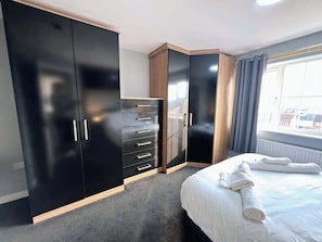 Un dormitorio con cama, armario y ventana con cortinas.