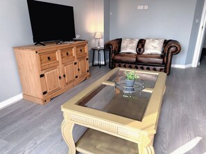A living room with a wooden cabinet, a leather sofa, and a glass-top coffee table. - Elegant 4BDR Home with Private Parking in Darfield (Darfield)