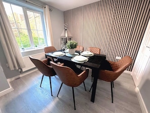 Un comedor con una mesa dispuesta para cuatro personas, rodeada de sillas, una planta en maceta y un muro a rayas.