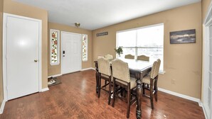 A dining room with a wooden table and chairs, a window with a view, and a door with a decorative window. - Grace Home (Houston)