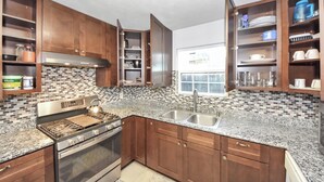 A kitchen with wooden cabinets, a stainless steel stove, a sink, and a window with a view. - Grace Home (Houston)