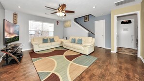 A living room with a sectional sofa, a ceiling fan, a flat-screen TV, and a wooden floor. - Grace Home (Houston)