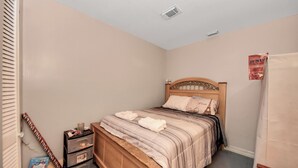 A bedroom with a wooden bed, a nightstand, a dresser, and a poster on the wall. - Grace Home (Houston)