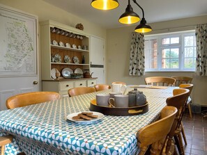 A dining area with a patterned tablecloth, wooden chairs, a buffet tray, and a map on the wall.