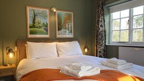 A neatly made bed with white linens, two framed landscape paintings, a window with curtains, and a bedside lamp. - Historic folly in Capability Brown park for family or friends groups (Malton)