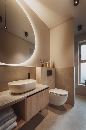 Une salle de bain moderne avec un grand lavabo ovale, des toilettes et un miroir incurvé.
