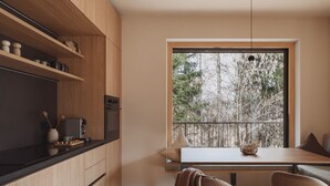 A modern kitchen with wooden cabinetry, a built-in oven, and a dining area with a table and chairs. - DAS AICH - Suite Sova (Aich-Assach)