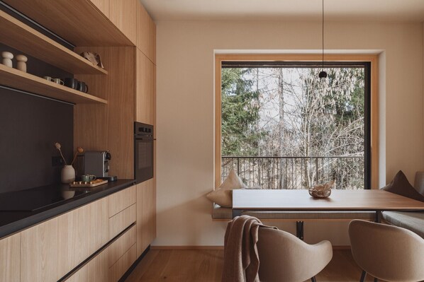 Une cuisine moderne avec des meubles en bois, un four encastré et un coin repas comprenant une table et des chaises.