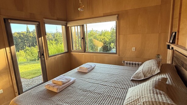 Ein Schlafzimmer mit einem großen Bett, zwei Fenstern und einer Pendelleuchte.
