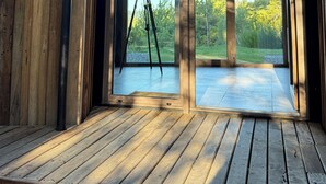 Ein Zimmer mit einem Teleskop auf einem Stativ, großen Glasschiebetüren und einer Holzterrasse.