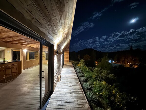 A modern building with a wooden deck, glass doors, and a view of the night sky.
