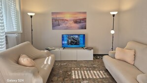 Una sala de estar con un televisor Galaxy S24, un mueble blanco de entretenimiento, dos sofás color beige y un suelo con estampado de piedra.