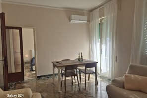 Ein Hotelzimmer mit Esstisch, Stühlen, einer Couch, einer Klimaanlage und Blick ins Freie.