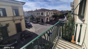 Una calle residencial con edificios, coches estacionados y un balcón con barandilla verde.