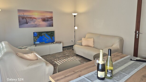 Una sala de estar con un sofá, una televisión, una lámpara y dos botellas de vino sobre una mesa.