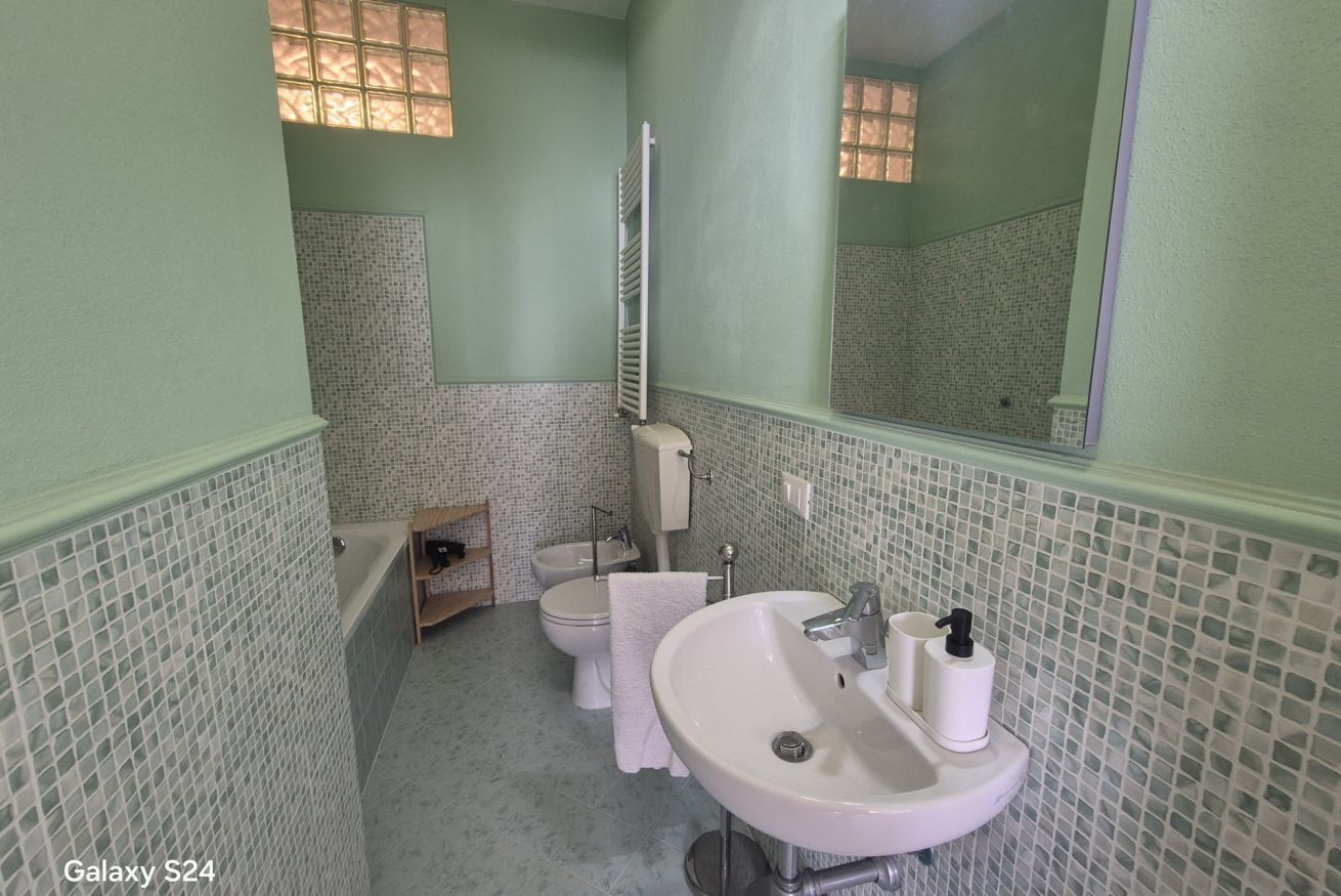 Un baño con un lavamanos blanco, dos inodoros, una ducha y un espejo.