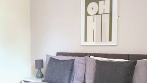 Una cama bien hecha con un edredón gris y blanco, un cabecero gris y un cuadro colgado en la pared con el texto 'OH HI'.