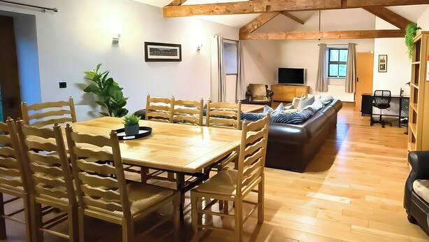 A spacious room with a wooden dining table, chairs, a sofa, and a television. - Old Corner Barn (Penrith)