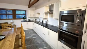 A modern kitchen with white cabinets, a black countertop, and stainless steel appliances including a microwave and oven. - Old Corner Barn (Penrith)