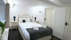 A neatly arranged bedroom with a bed, bedside tables, a lamp, a wardrobe, and a plant. - Old Corner Barn (Penrith)