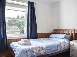 Quarto com cama de madeira, mesa de cabeceira, janela com cortinas e vista para árvores e um edifício lá fora.