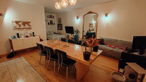 En moderne stue med et træspisebord, sorte stole, en sofa, et fjernsyn og et stort spejl.