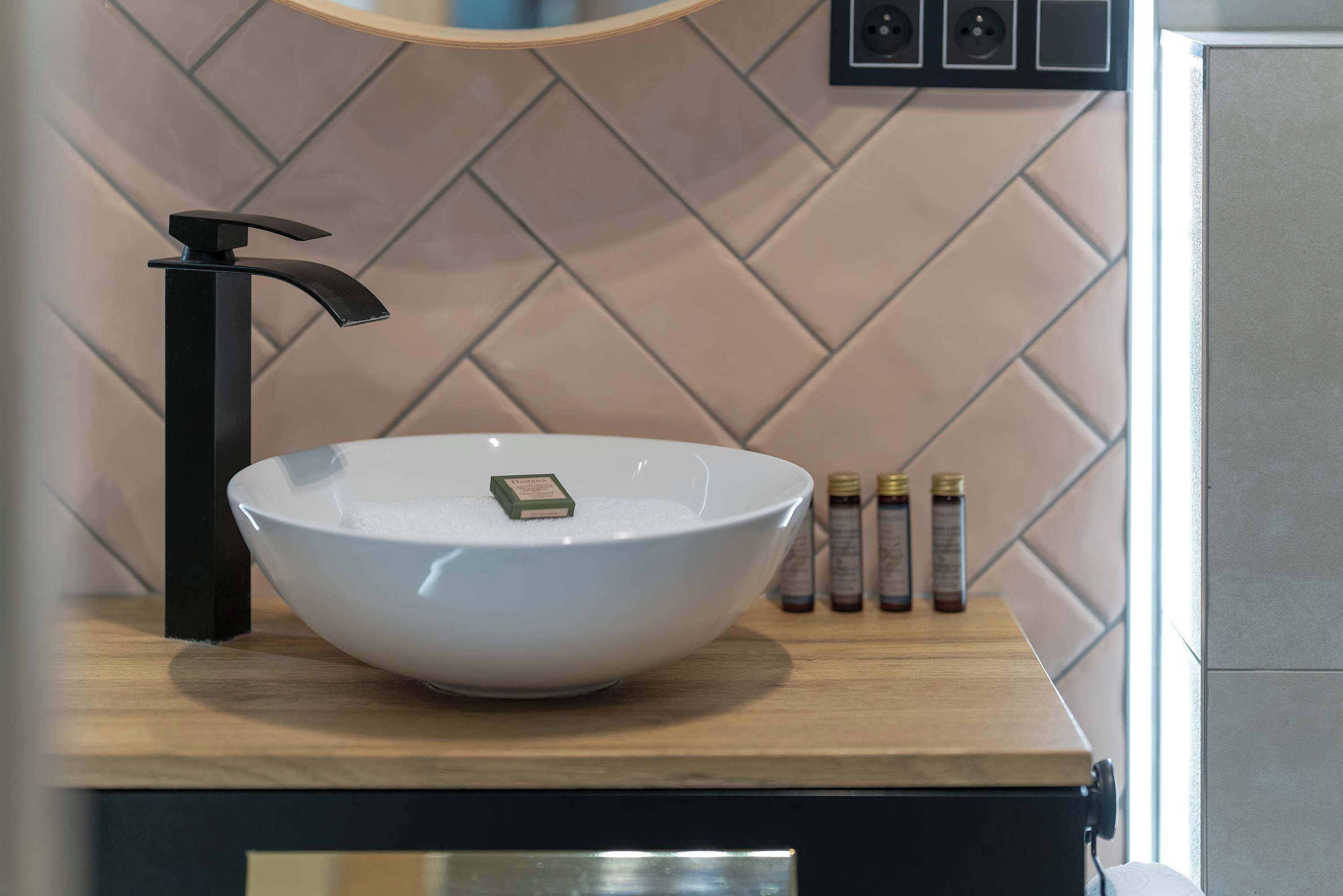 Une salle de bain moderne avec un lavabo sur colonne blanc, un robinet noir et un plan de toilette en bois.
