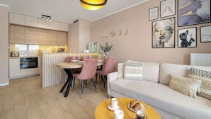 Una sala de estar moderna con un sofá, una zona de comedor con sillas rosas y una cocina al fondo.
