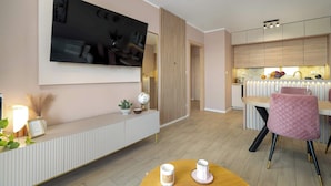 Una sala de estar moderna con un televisor de pantalla plana, una consola blanca, una silla rosa y una mesa de comedor de madera.