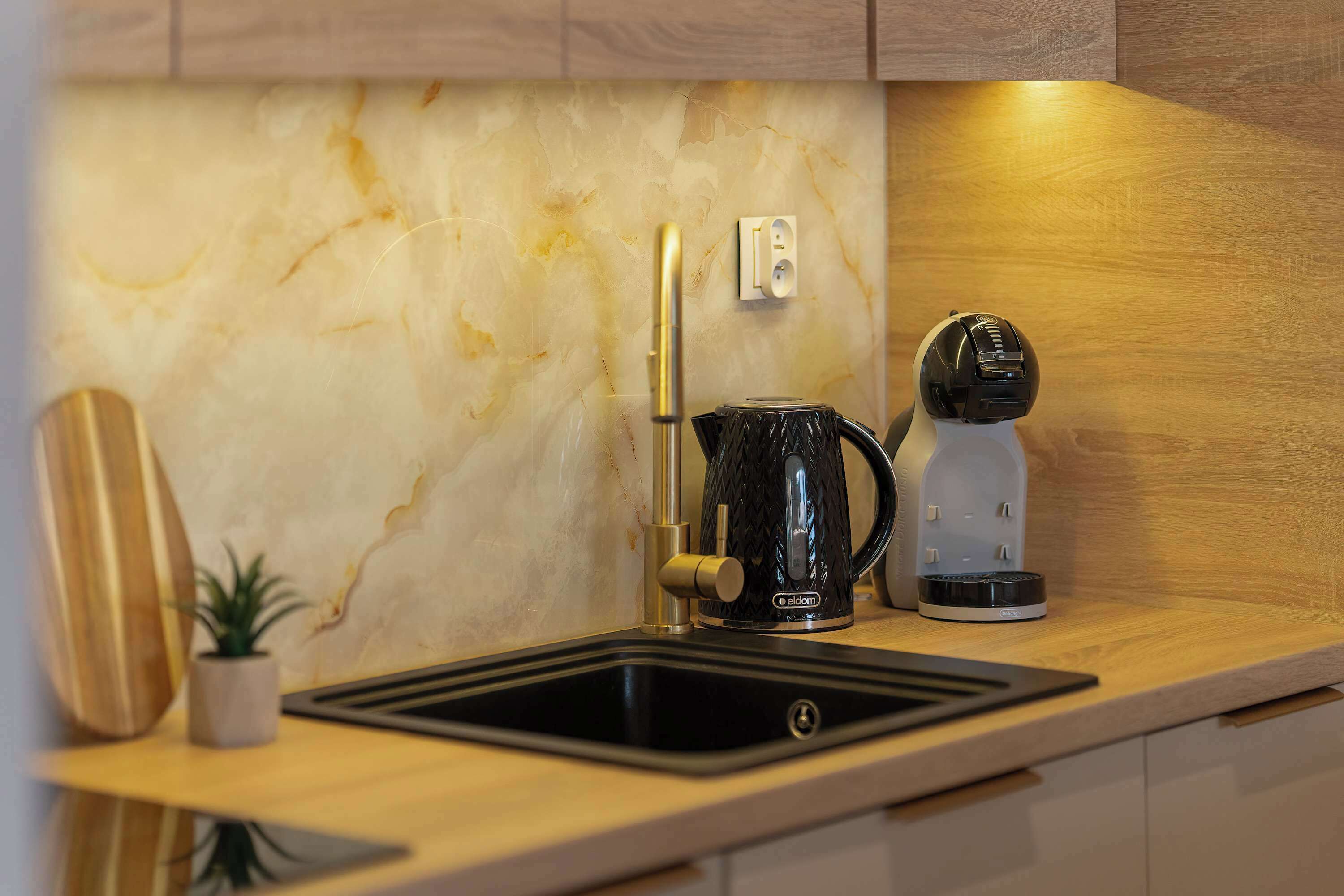 A kitchen with a marble backsplash, a coffee maker, a knife block, and a small potted plant.