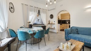 Un coin repas avec une table ronde, des chaises de couleur turquoise, une table basse en bois ornée de bougies et un canapé bleu.
