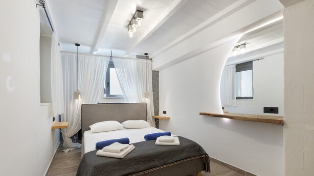 Une chambre à coucher moderne avec un grand lit, des tables de chevet, un miroir et une fenêtre avec des rideaux.