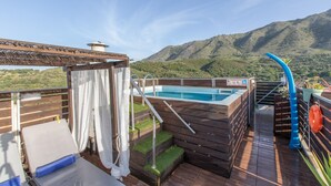 Een houten terras met een jacuzzi, een glijbaan en een zwembad.