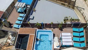 Piscina en la azotea con sillas de descanso, jacuzzi y plantas en macetas.