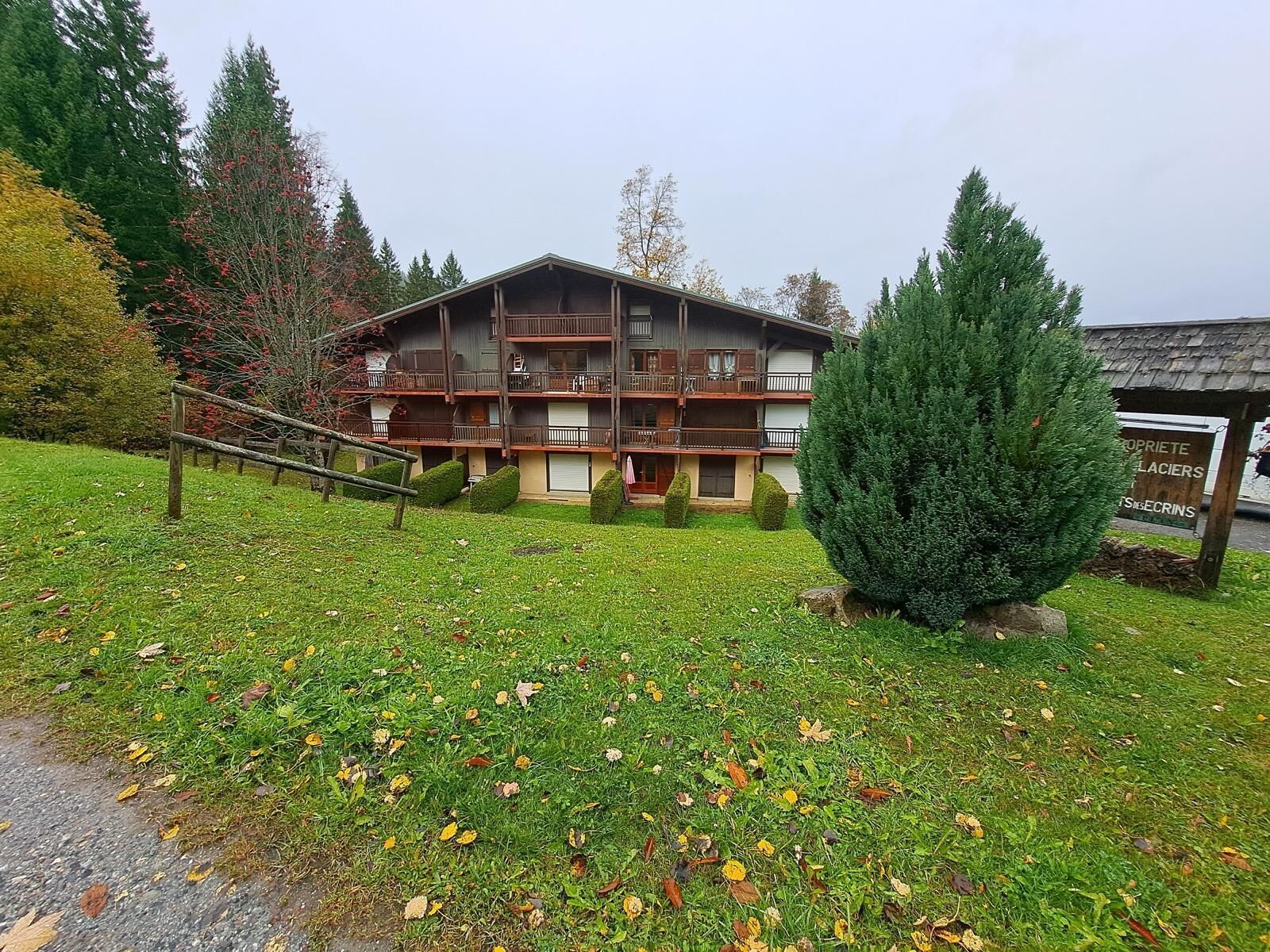 A multi-story building with balconies, surrounded by a grassy area with trees and a signboard.