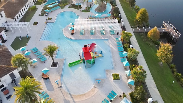 Area piscina di un resort con diverse scivoli acquatici, lettini e un pontile sul mare.