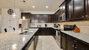 Cucina con piani in granito, mobili in legno scuro, elettrodomestici in acciaio inossidabile e illuminazione a sospensione.