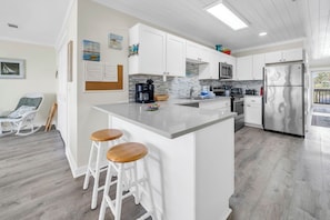A modern kitchen with white cabinets, a stainless steel refrigerator, and a bar area with stools. - 🏖️Stunning Gulf Views | Pet Friendly | Sands of Laguna B-1🏖️ (Panama City Beach)