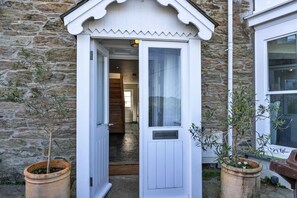 A white door with a small porch, a stone wall, and potted plants. - Captains No. 9 (Falmouth)