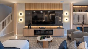 Un salon moderne doté d’un grand téléviseur à écran plat, d’un meuble de rangement en bois et d’un mobilier confortable.