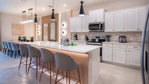 Une cuisine moderne dotée d’un grand îlot central, de tabourets de bar, de meubles blancs et d’appareils électroménagers en acier inoxydable.