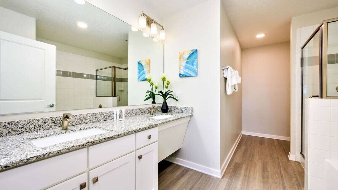 Een moderne badkamer met een grote spiegel, een granieten aanrechtblad, witte kastjes en een douchehoek.