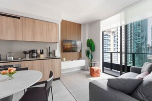 A modern kitchen with wooden cabinets, a dining area with a round table and chairs, a large window with a city view, and a grey sofa in a living area. - Miami 167 - One Bedroom Apartment, Sleeps 5 (Miami)