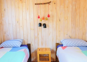 Una habitación de madera con dos camas, una mesita de madera y dos lámparas fijadas a la pared.
