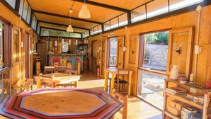 A spacious room with a large octagonal table, wooden furniture, and large windows allowing natural light. - Glamping Tilcara El Obrador (Tilcara)