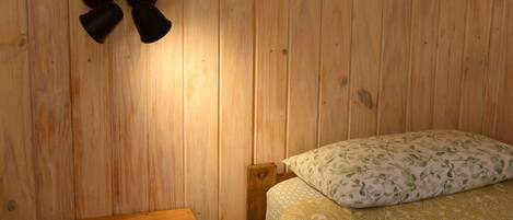 Een houten kamer met een bed, een klein houten tafeltje en loshangende kwastjes.